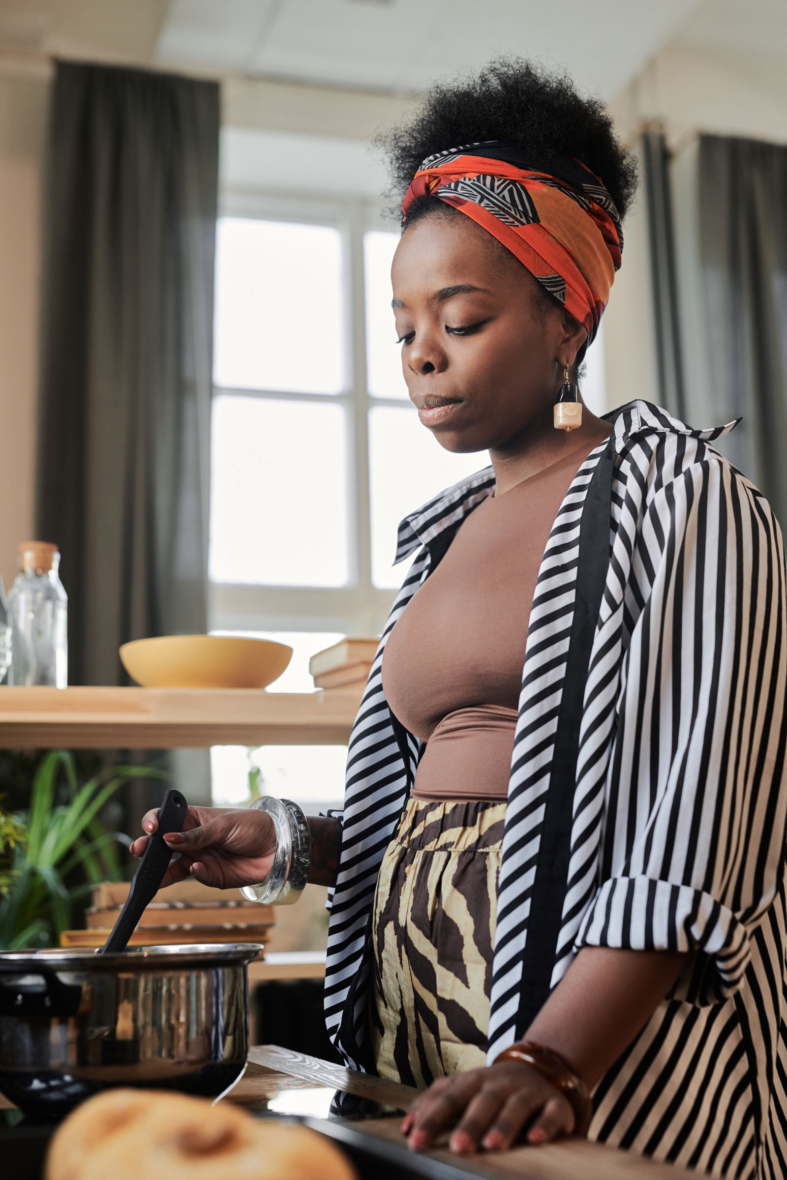 A Black woman preparing food on a lit gas stove at home.