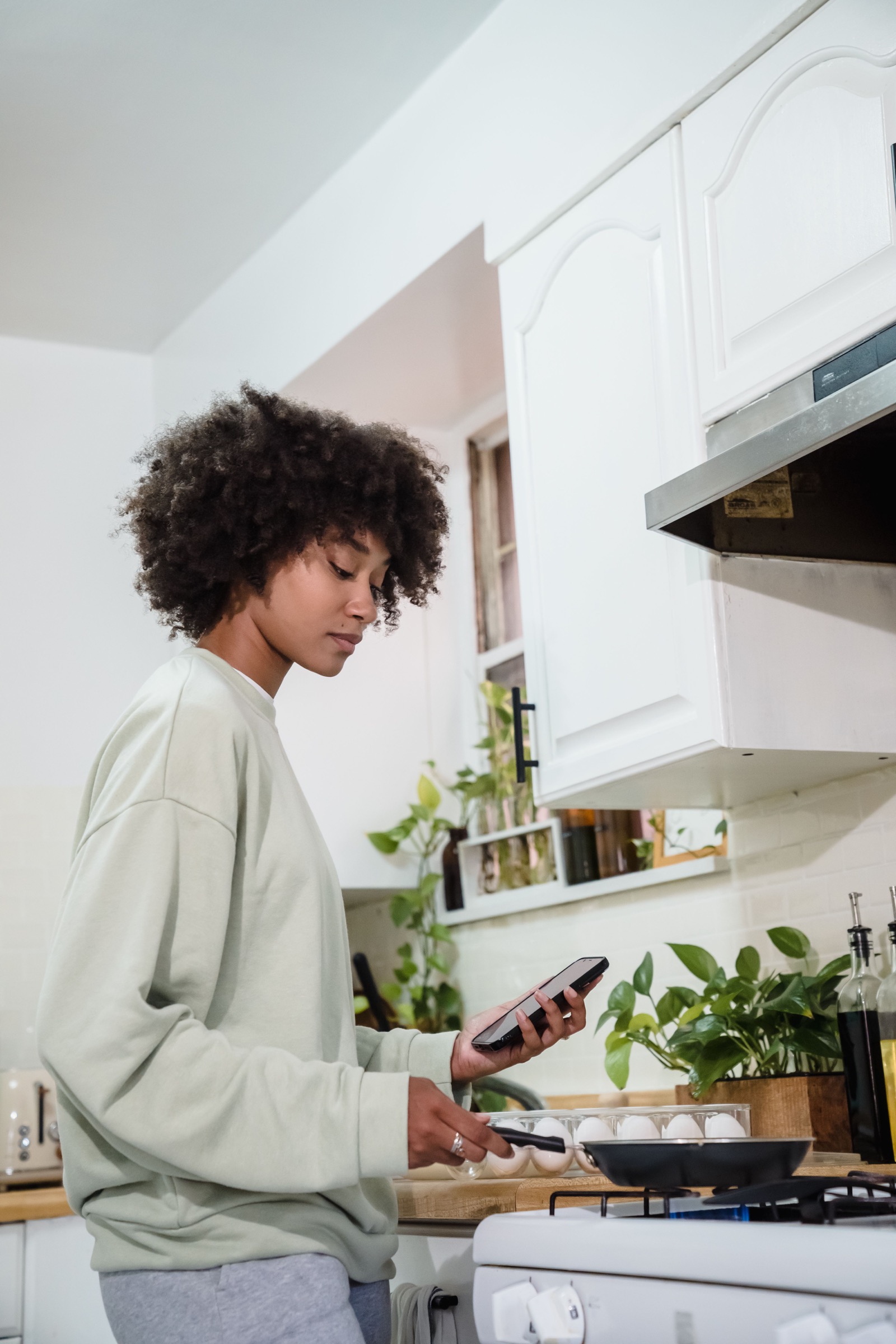 A Black woman checking her phone beside a lit gas stove.